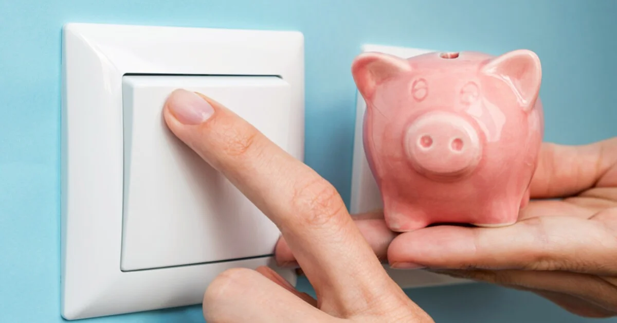 a person turning a light switch off with a piggybank next to it