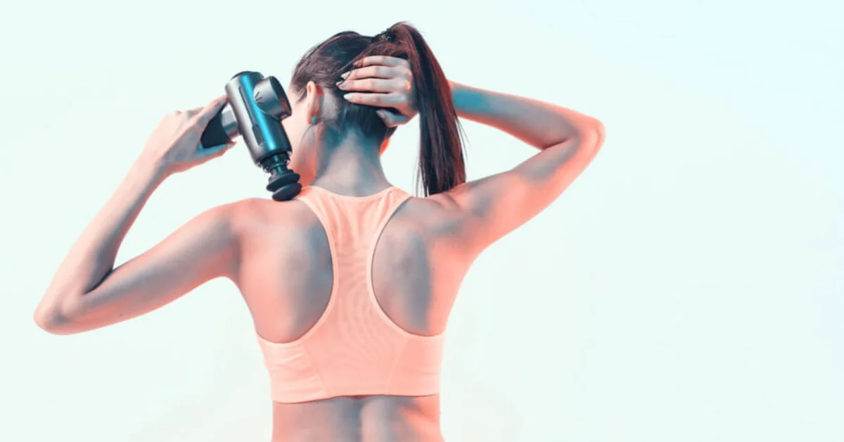 a young athletic woman using a massage gun on her back