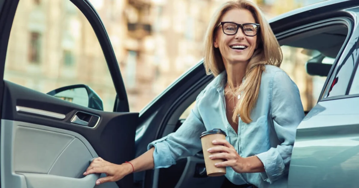 a woman smiling in a car with a coffee cup