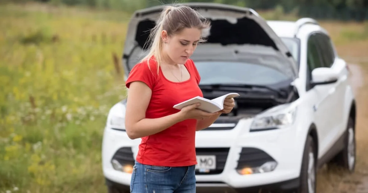 a young woman stood by the side of the road reading a car manual