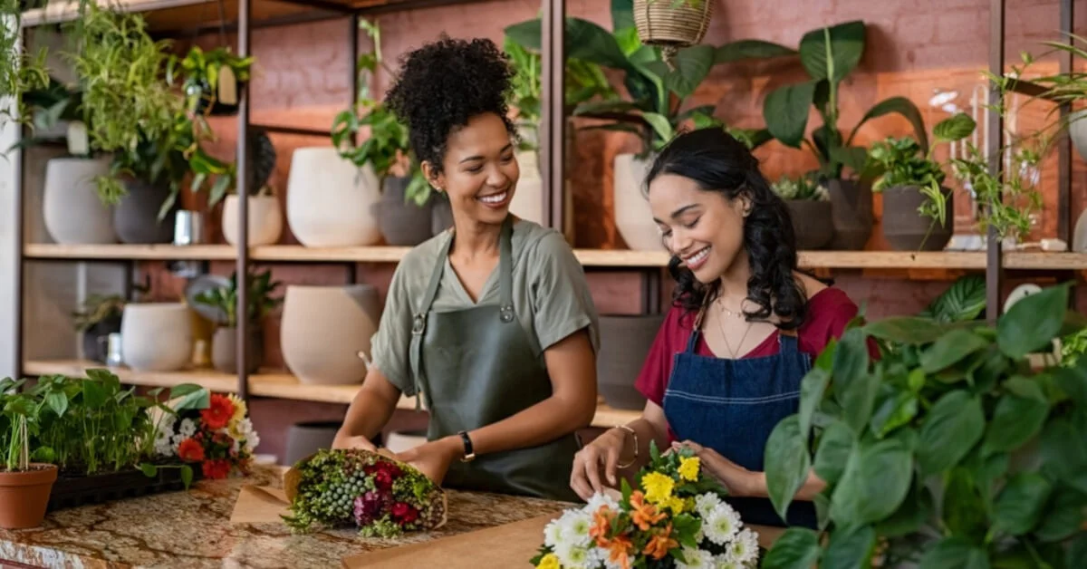 two women smiling sorting a flower arrangement