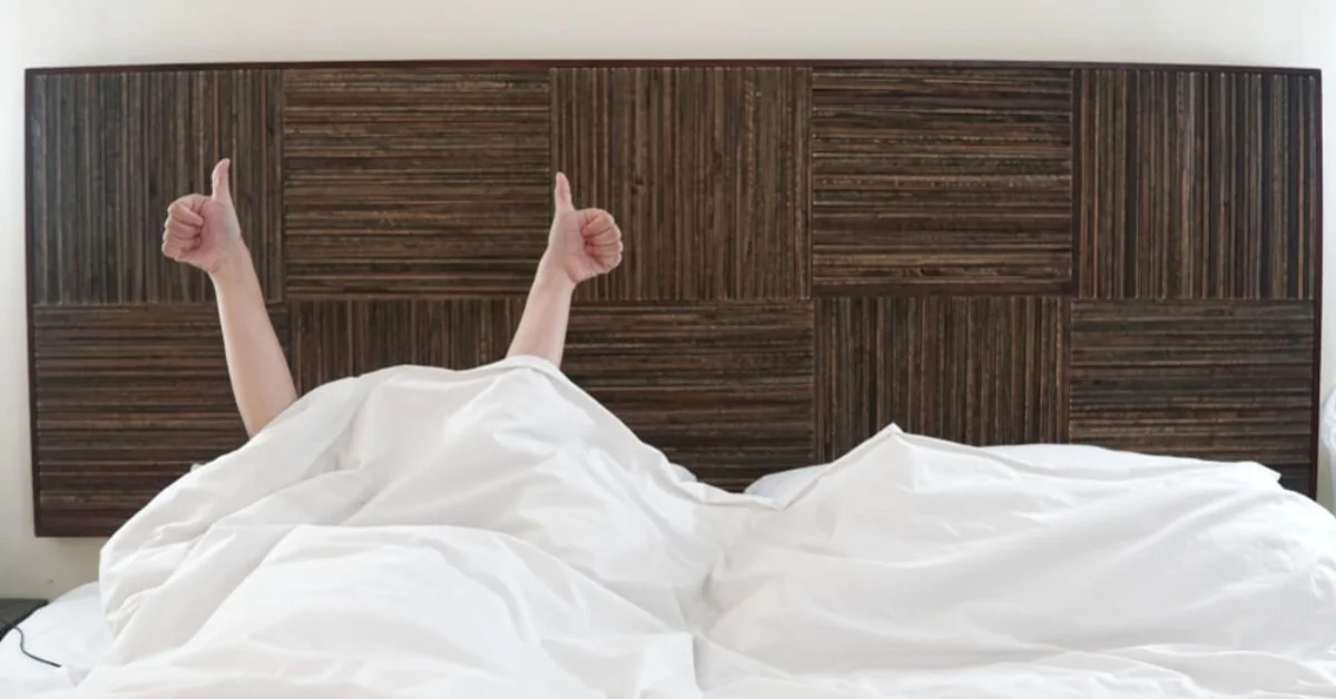 person laid in bed under the duvet with thumbs up in the air