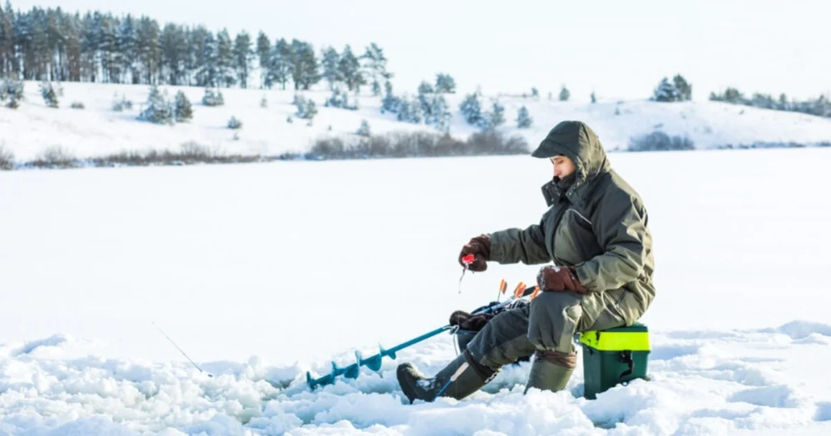 a man sat on a box in the snow fishing