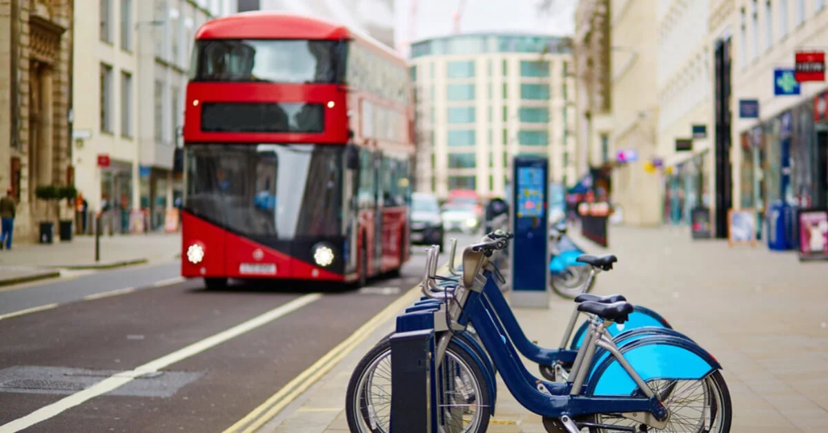 a red bus in london on a busy street with bikes chained up