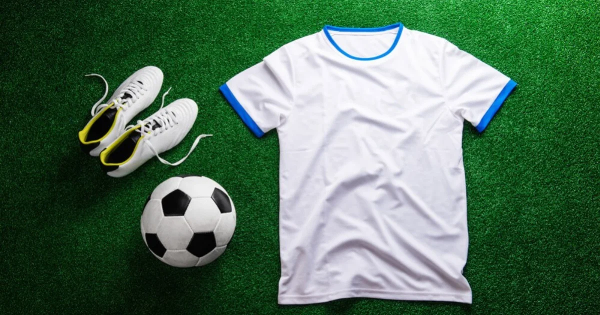 a football shirt laid on grass next to a football and pair of boots