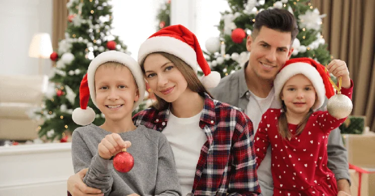 A family wearing Christmas hats sat Infront of a Christmas tree