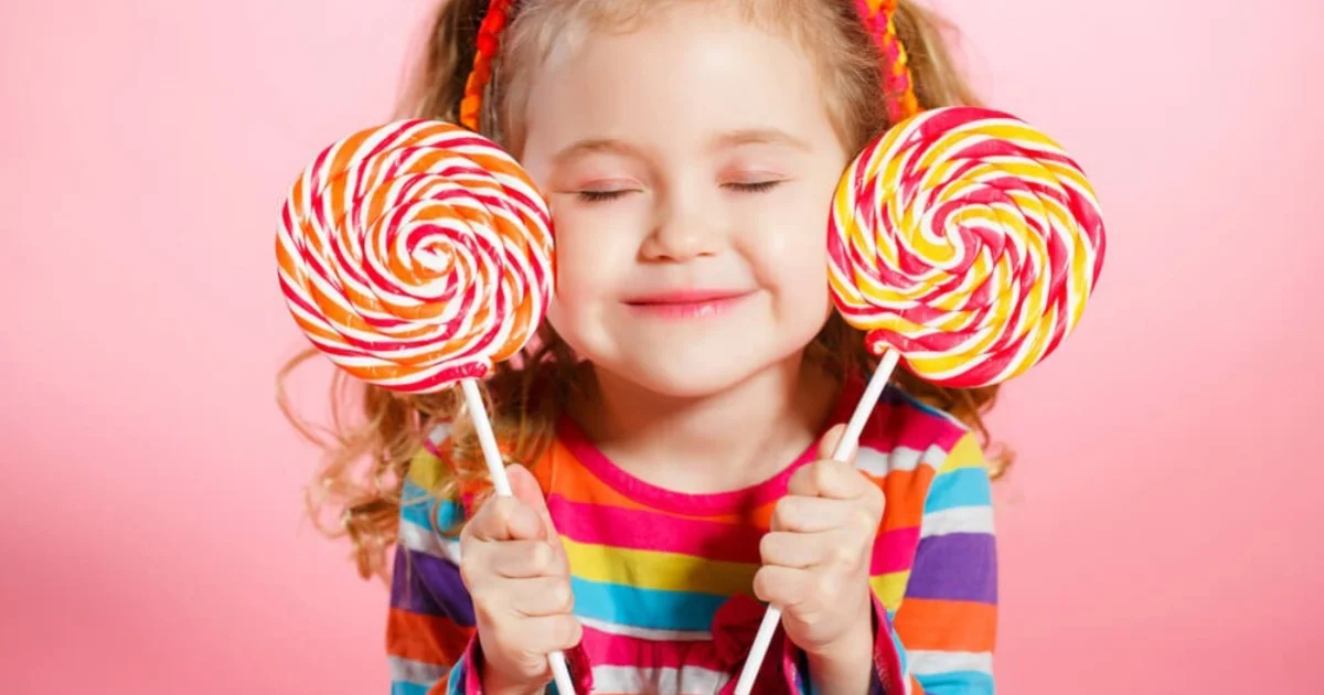 a young girl smiling with two large candy sticks