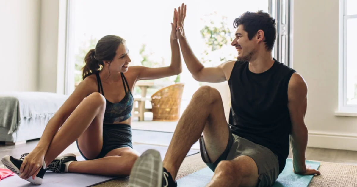 young couple doing yoga at home giving each other a highfive