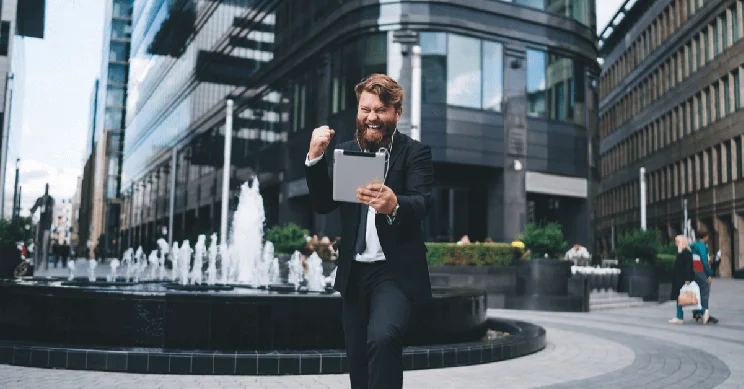 An excited man in a suit holding an ipad, punching the air