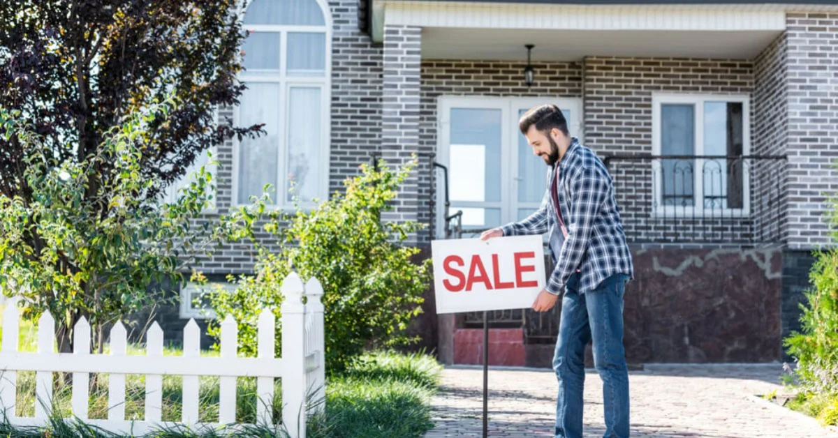 a man holding a sale sign up in front of his home