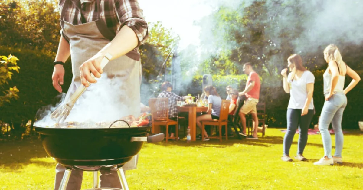 a man bbqing with people sat eating behind him