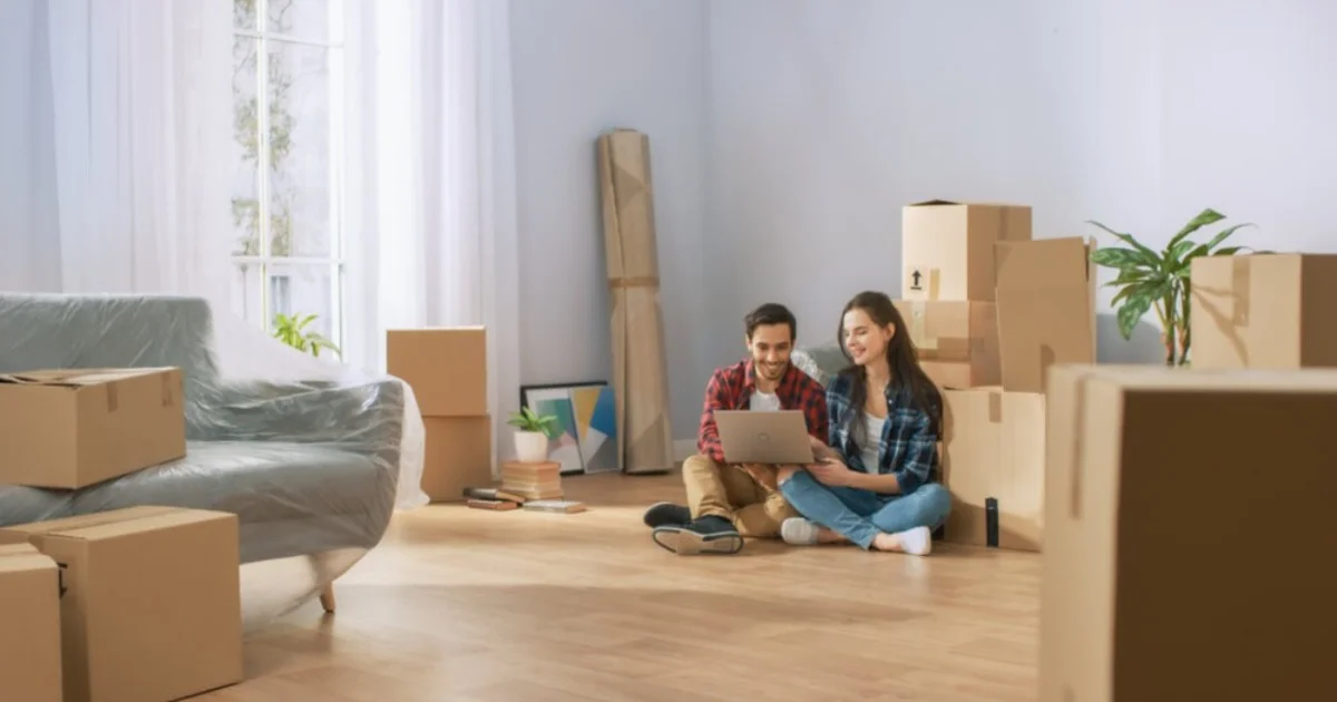 young couple sat in an empty home full of cardboard boxes