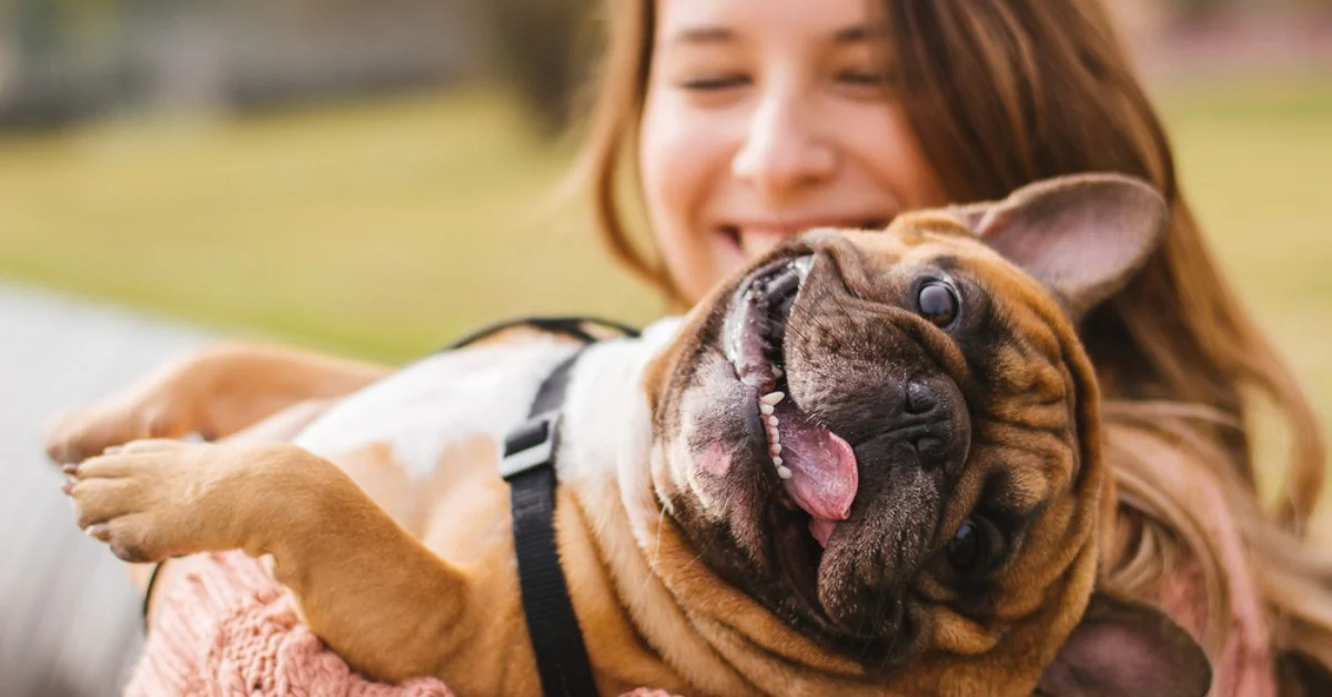 a woman holding a small dog looking very happy in a park